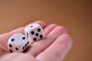 White dice lie on an open palm close-up on a brown background with a copy space. Playing table...