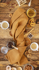 Fototapeta na wymiar A wooden table with a folded kitchen towel around which fruit chips, dried fruits, nuts, honey and two cups of coffee. Healthy snack and eco friendly dining accessories. Healthy coffee time