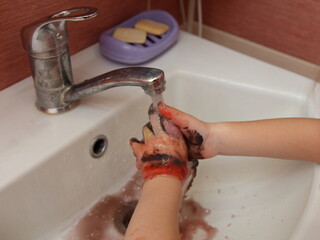 A child washes his hands of paint after drawing with water stream from the tap on soap background in the bathroom close-up, home hygiene