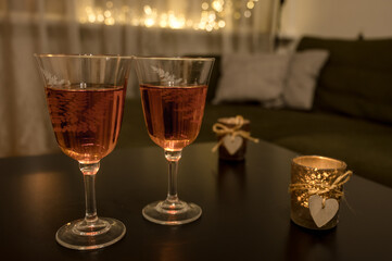 Couple of glasses with wine and candle with wooden heart on black table. Romantic composition. Modern interior. Close-up. Bokeh lights.
