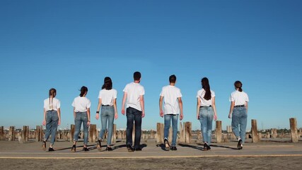 Young men in white T-shirts are slowly walking along the sand into the distance to the posts from the pier. Shooting at 205 fps.
