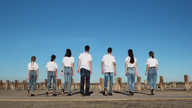 Young men in white T-shirts are slowly walking along the sand into the distance to the posts from the pier. Shooting at 205 fps.