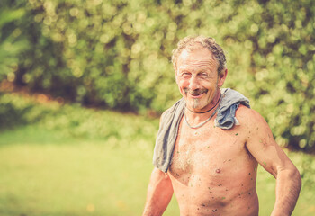 Portrait of smiling shirtless gardener in front of green plants in the garden..