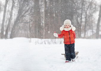 Fototapeta na wymiar a little girl in a fluffy hat walks on a snowy winter day