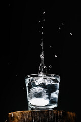 Pure fresh water in glass, an effervescent tablet with vitamin C falls into the glass, splashing over the water, dark background with copy space for text, selective focus. Close-up, vertical frame