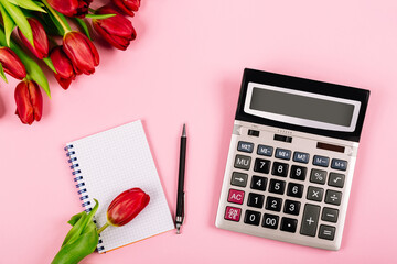 Bouquet of red tulips on pink paper background with calculator, spiral notebook and pen are a template for advertising or visualization of blog with copy space for text. Business holiday. Certificate