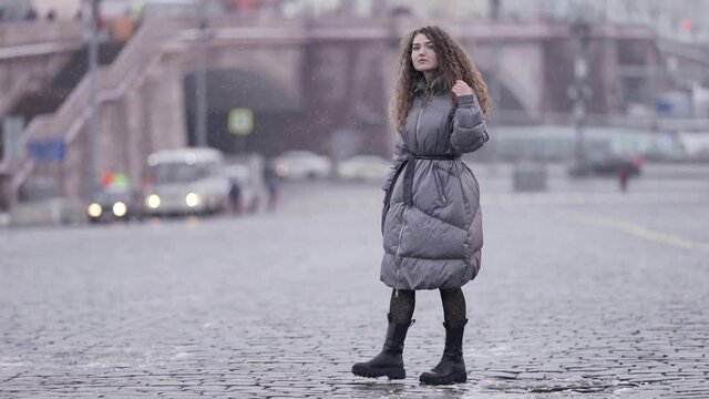 snowless winter in big city, young woman dressed down jacket, strolling alone