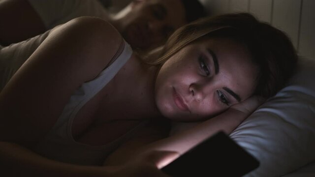 The woman lying in the bed and using smartphone