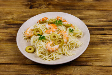 Spaghetti pasta with prawns, green olives and parsley on wooden table