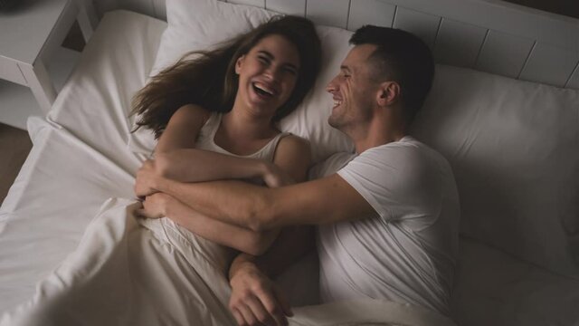 The man and woman are tickling each other in the bed