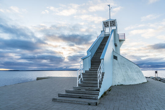 Lighthouse in Nallikari, Oulu, Finland. Scenic evening skyline over deep blue Baltic sea with stunning clouds at sunset. Beautiful stairs to observation tower at the end of a paved dock. ..