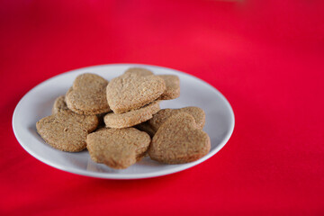Galletas con forma de corazón sobre un plato blanco y fondo rojo, vista 45º