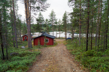 Stunning remote red wooden cabin in Inari, Lapland, Finland surrounded by idyllic green pine forest and romantic lake. Perfect cottage for relaxing