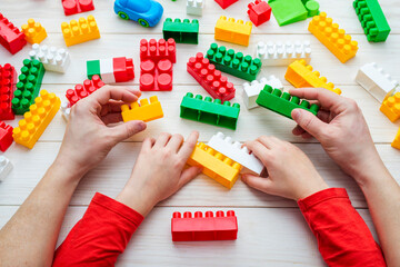 Top view on childs and fathers hands playing with colorful plastic bricks. Father with his toddler son playing with colorful plastic blocks
