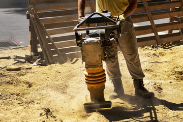 Construction worker compacting soil in house foundation using compactor. Work with tamping machine!