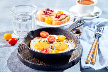 Fried eggs. Fried eggs from two eggs in cast-iron pan with cherry tomatoes and microgreens, toast and cup of coffee. Sunny morning breakfast concept
