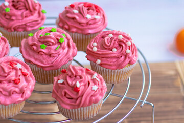muffins with scarlet cream and decor , pearls and red and green stars. holiday cupcakes on a metal stand on a wooden background. High quality photo