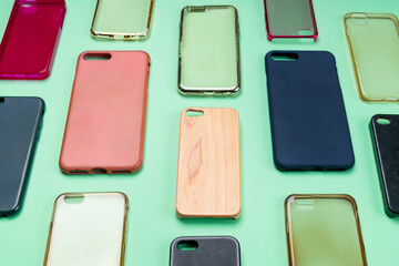 Pile of multicolored plastic back covers for mobile phone. Choice of smart phone protector accessories on green background. A lot of silicone phone backs or skins next to each other