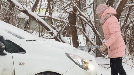 Winter problems of car drivers. Machine, covered with snow. A girl brushing snow from the car....