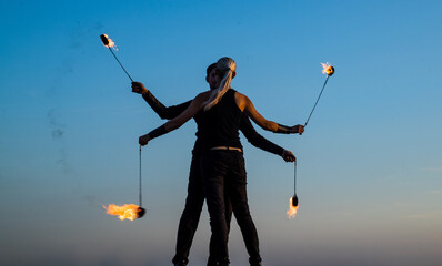 couple in love dance while spinning burning poi blue sky outdoors, fire show