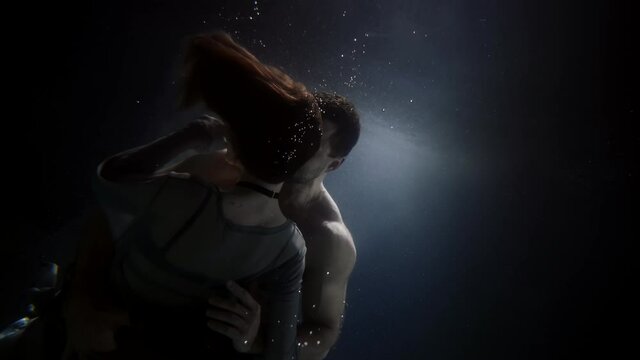 muscular man is hugging young woman underwater, loving couple inside swimming pool