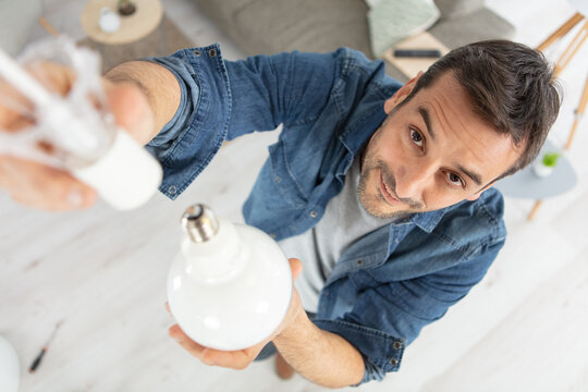 Asian Man Changing Light Bulb In Coffee Shop