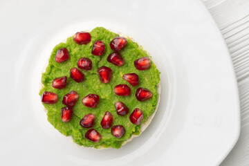 Close up rice cakes with avocado mash and pomegranate seeds in white plate top view