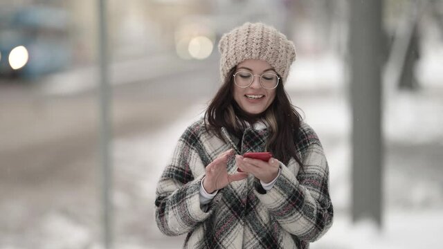 young woman is walking in city and viewing social nets in smartphone, chatting online and smiling