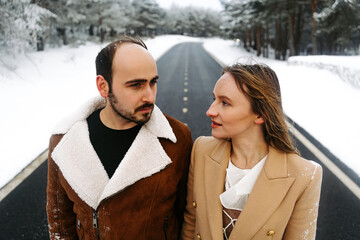pareja joven abrigada feliz abrazándose sacando la lengua en el exterior en bosque en un día frio...