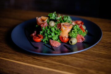 Fresh salad with salmon, tomatoes, lettuce, grapefruit, on a black plate