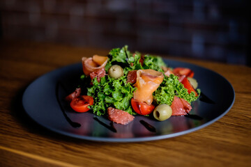 Fresh salad with salmon, tomatoes, lettuce, grapefruit, on a black plate