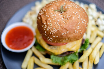 Fast food and unhealthy eating concept, french fries, ketchup and burger on the black plate
