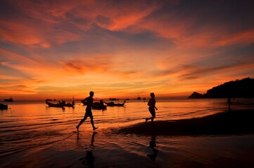 Fototapeta premium Tropical romantic paradise: sunset at the seaside - dark silhouettes of palm trees and orange cloudy sky