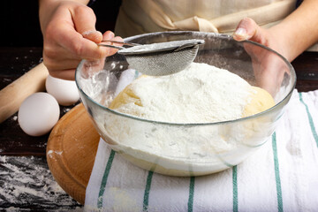 Woman baker kneads yeast dough. Sifting flour through a sieve. Making bread dough. Work at the bakery.