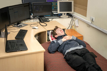  Tired guy sleeps in front of monitors in the office. The monitoring operator is lying on the bed. A man from the technical department sleeps on a bed at his workplace.