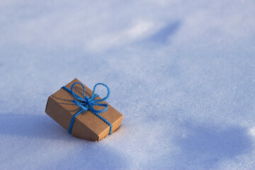 gift box with blue lace bow on the snow in sunny winter day - close up with copy space, merry christmas and happy new year, winter holidays and shopping