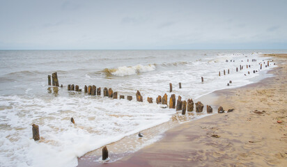 The waves hit the remains of a beach pier peeking out of the sea