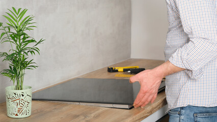 A young repairman installs a black induction hob in a modern white Scandinavian style kitchen with...