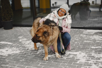 Cute african girl in a winter park. Woman in a pink coat. Lady with a dog.