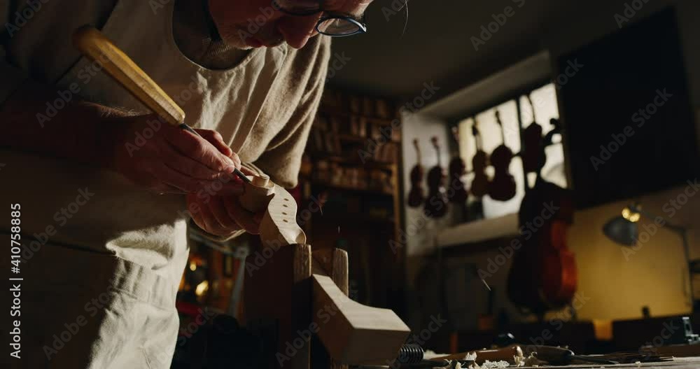 Poster Cinematic shot of experienced master artisan luthier painstaking detail work on fine quality wood violin in creative workshop.Concept of spiritual instrument,handmade, art, orchestra, artisan, passion