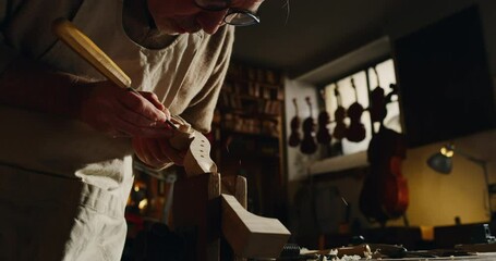 Cinematic shot of experienced master artisan luthier painstaking detail work on fine quality wood violin in creative workshop.Concept of spiritual instrument,handmade, art, orchestra, artisan, passion