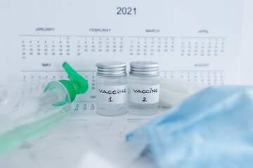 covid-19 vaccine against the pandemic, ampoules with Vaccine 1 and Vaccine 2 labels side by side next to 2021 yearly calendar and mask gloves and sanitizer