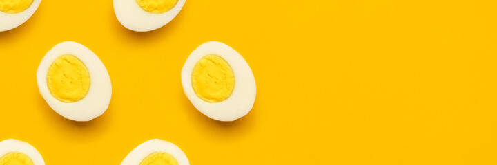 Banner with fresh chicken boiled half cut eggs pattern on yellow background. Healthy food or Happy Easter creative minimal concept. Flat lay, top view