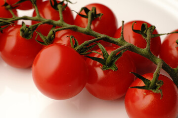 Small red tomatoes on a branch on a white plate. Dietary nutrition.