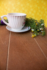 TÉ DE MANZANILLA EN TAZA DE PORCELANA SOBRE MADERA Y FONDO AMARILLO