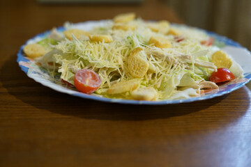A salad on a plate sits on an old wooden table. Side view.