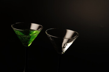 Two glasses with a green cocktail on a black background. One glass is full and the other is empty