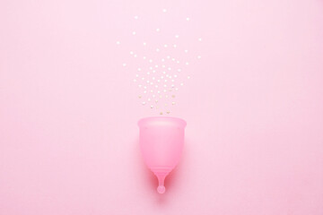 Menstrual cup with glitter on pink background. Alternative feminine hygiene product during the period. Women health concept