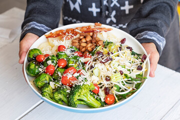 A person holding a very healthy homemade green salad plate with high protein with soybean germs, spinach and cherry tomato