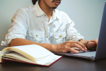 A young man with mustache wearing a white shirt looking and typing on his laptop. Selective focus shot. Vintage filter applied. Copy space. Business concept.